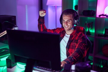 Young caucasian man streamer playing video game with winner expression at gaming room - obrazy, fototapety, plakaty