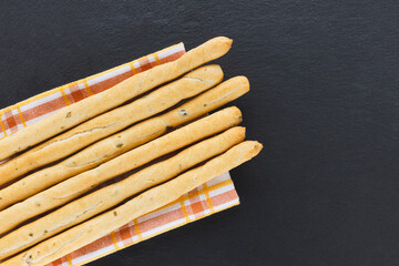 Fresh Italian Grissini Breadsticks served on black background. Dry baked bread with olive pieces on slate plate. Top view, copy space