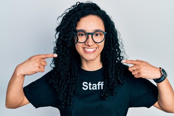 Young hispanic woman with curly hair wearing staff t shirt smiling cheerful showing and pointing with fingers teeth and mouth. dental health concept.