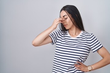 Young brunette woman wearing striped t shirt tired rubbing nose and eyes feeling fatigue and headache. stress and frustration concept.