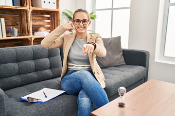 Young woman working at consultation office smiling doing talking on the telephone gesture and pointing to you. call me.