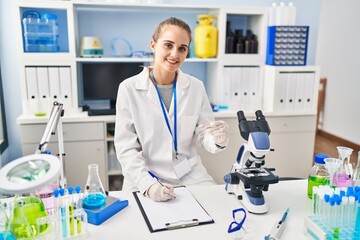 Young blonde woman wearing scientist uniform writing on checklist at laboratory