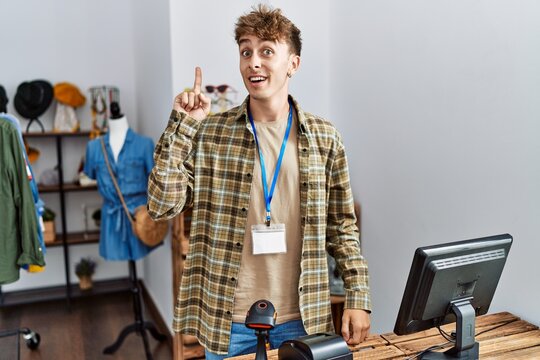 Young caucasian man working as manager at retail boutique pointing finger up with successful idea. exited and happy. number one.