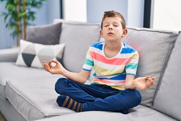 Blond child doing yoga exercise sitting on sofa at home