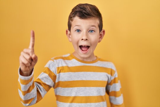 Young Caucasian Kid Standing Over Yellow Background Pointing Finger Up With Successful Idea. Exited And Happy. Number One.