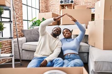 Man and woman couple doing house gesture sitting on floor at new home