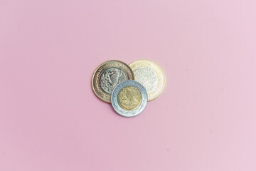 Dos monedas de 10 pesos mexicanos y moneda de 2 pesos mexicanos sobre fondo rosa.