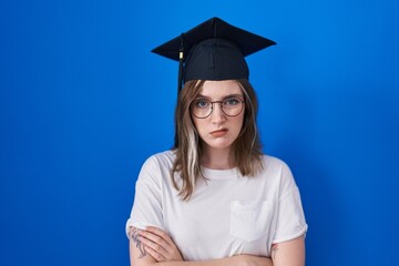 Blonde caucasian woman wearing graduation cap skeptic and nervous, disapproving expression on face with crossed arms. negative person.