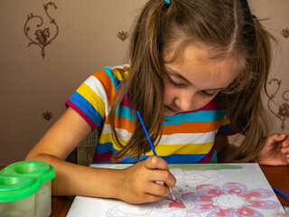 A little girl enthusiastically paints with paints on a white canvas.
