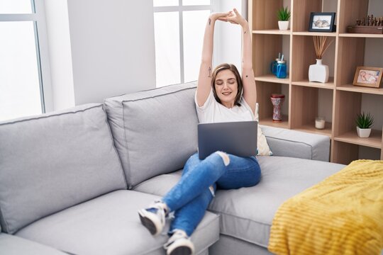 Young woman using laptop stretching arms at home