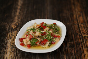 Roasted red pepper salad with cheese, herbs, and garlic. Delicious grilled peppers on a white plate on wooden background. Traditional Turkish appetizer (meze). 