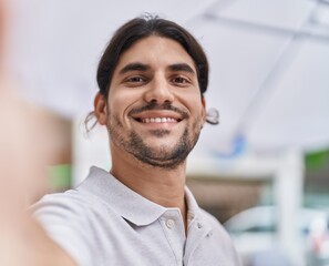 Fototapeta premium Young hispanic man smiling confident making selfie by the camera at street