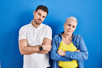 Young brazilian mother and son standing over blue background looking sleepy and tired, exhausted for fatigue and hangover, lazy eyes in the morning.