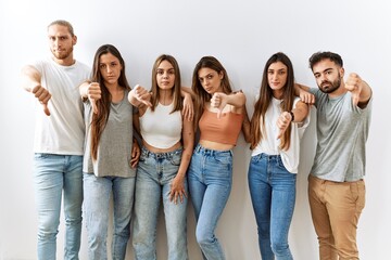 Obraz premium Group of young friends standing together over isolated background looking unhappy and angry showing rejection and negative with thumbs down gesture. bad expression.