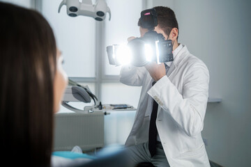 Handsome dentist making photo of female patient's smile after treatment. Special camera with flash...