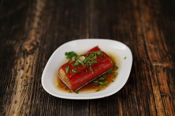 Roasted red peppers stuffed with cheese, herbs, and garlic. Delicious grill peppers on a white plate on wooden background. Traditional Turkish appetizer (meze). 