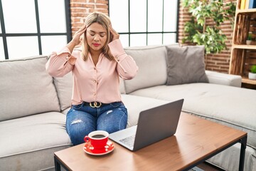 Young hispanic woman using laptop sitting on the sofa at home with hand on head for pain in head because stress. suffering migraine.