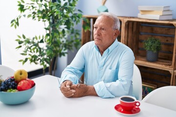 Senior grey-haired man drinking coffee sitting on table at home