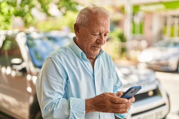 Obraz premium Senior grey-haired man smiling confident using smartphone at street