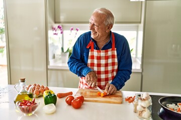 Senior man smiling confident cutting carrot at kitchen