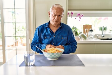 Senior man with grey hair eating pasta spaghetti at home depressed and worry for distress, crying angry and afraid. sad expression.