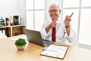 Senior man working at the office using computer laptop smiling and looking at the camera pointing with two hands and fingers to the side.