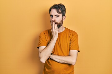 Caucasian man with beard wearing casual yellow t shirt bored yawning tired covering mouth with hand. restless and sleepiness.