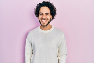 Handsome hispanic man wearing casual white sweater with a happy and cool smile on face. lucky...