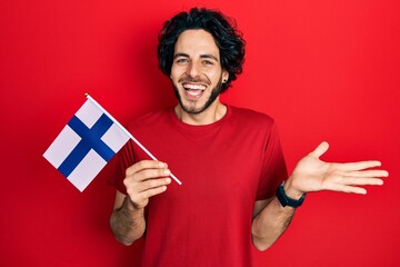 Handsome hispanic man holding finland flag celebrating achievement with happy smile and winner expression with raised hand