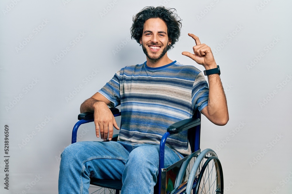 Sticker handsome hispanic man sitting on wheelchair smiling and confident gesturing with hand doing small si