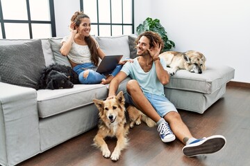 Young hispanic couple with dogs relaxing at home smiling with hand over ear listening an hearing to...
