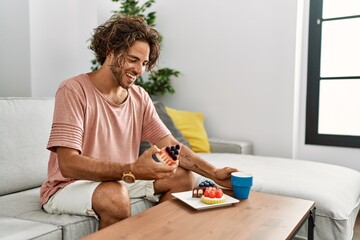 Young hispanic man having breakfast sitting on the sofa at home.