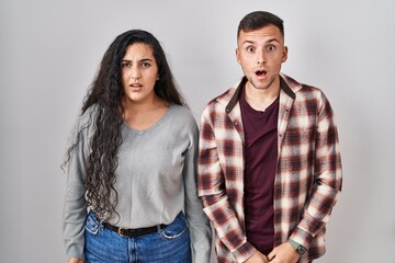 Young hispanic couple standing over white background afraid and shocked with surprise and amazed expression, fear and excited face.