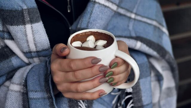 A woman holds a mug of hot cocoa with marshmallows and chocolate