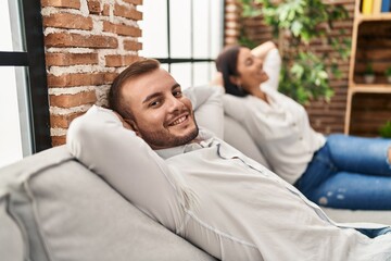 Man and woman couple relaxed with hands on head sitting on sofa at home