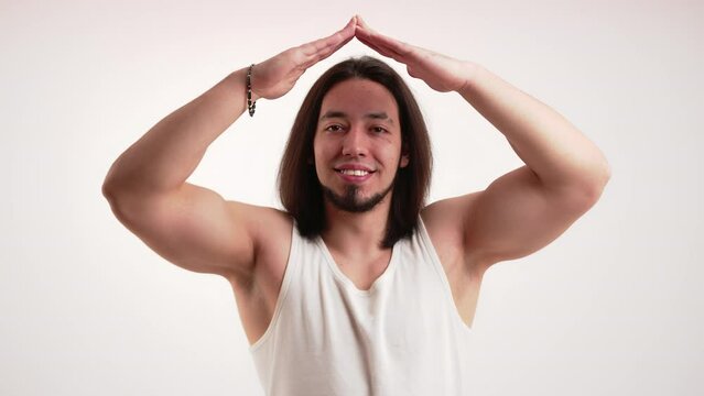 White bodybuilder wearing white tanktop holding arms above head in shape of roof looking into camera smiling. House gesture. Isolated. High quality 4k footage