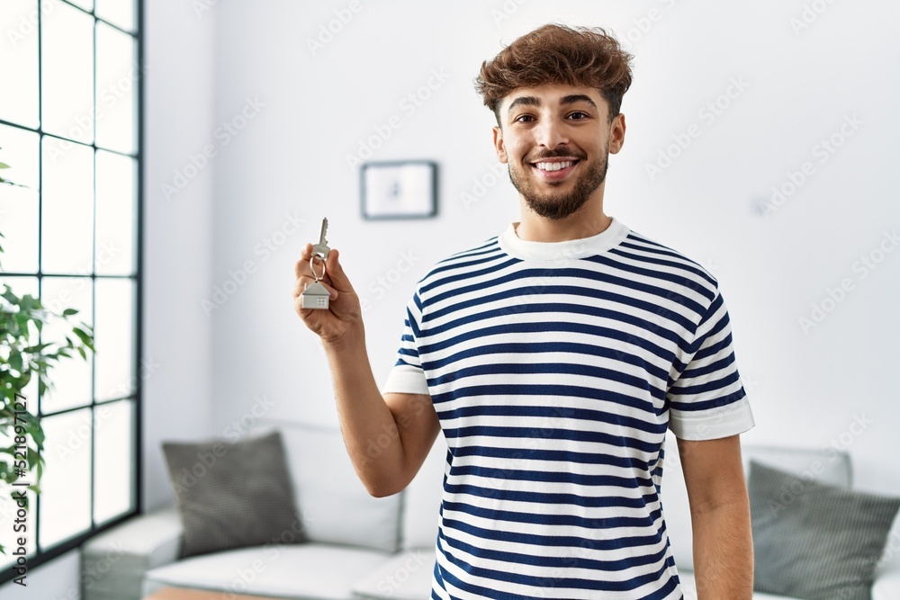 Sticker young arab man smiling confident holding key of new house at home