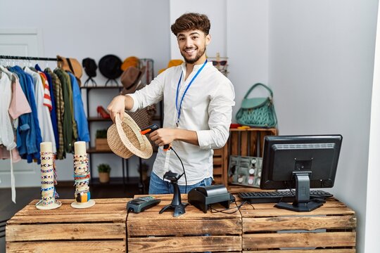 Young arab man smiling confident scanning hat using barcode reader at clothing store