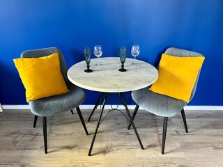 A stylish dining area - a table with two chairs with decor and blue wall in the background