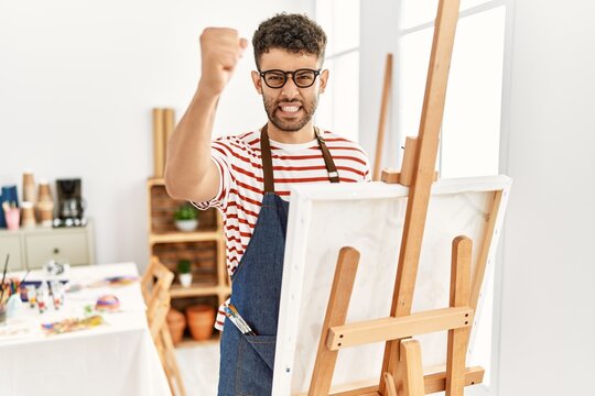 Arab young man at art studio angry and mad raising fist frustrated and furious while shouting with anger. rage and aggressive concept.