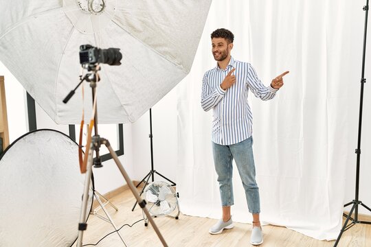 Arab young man posing as model at photography studio smiling and looking at the camera pointing with two hands and fingers to the side.