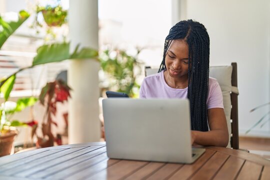 African american woman using laptop and touchpad sitting on table at home terrace
