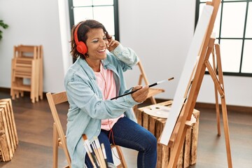 Middle age hispanic artist woman listening to music drawing at art studio.