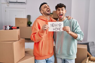 Young hispanic gay couple moving to a new home smiling and laughing hard out loud because funny crazy joke.