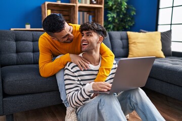 Fototapeta premium Two man couple using laptop sitting on sofa at home