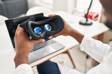 Young african american man wearing doctor uniform holding virtual reality glasses at clinic