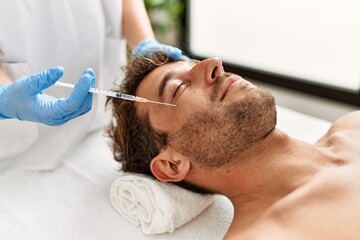 Young hispanic man having facial anti-aging treatment at beauty center