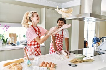 Young couple smiling happy cooking dough at kitchen.