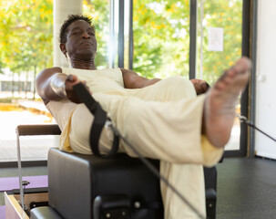 African-american man doing exercises on pilates reformer during training in gym.