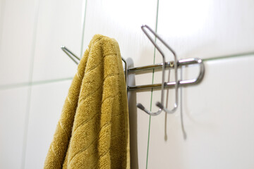 Defocus mustard towel hanging on hook. Metal sticky towels hanger for bathroom tiled wall. Closeup mustard towel hanging on the rack in the bathroom. Out of focus